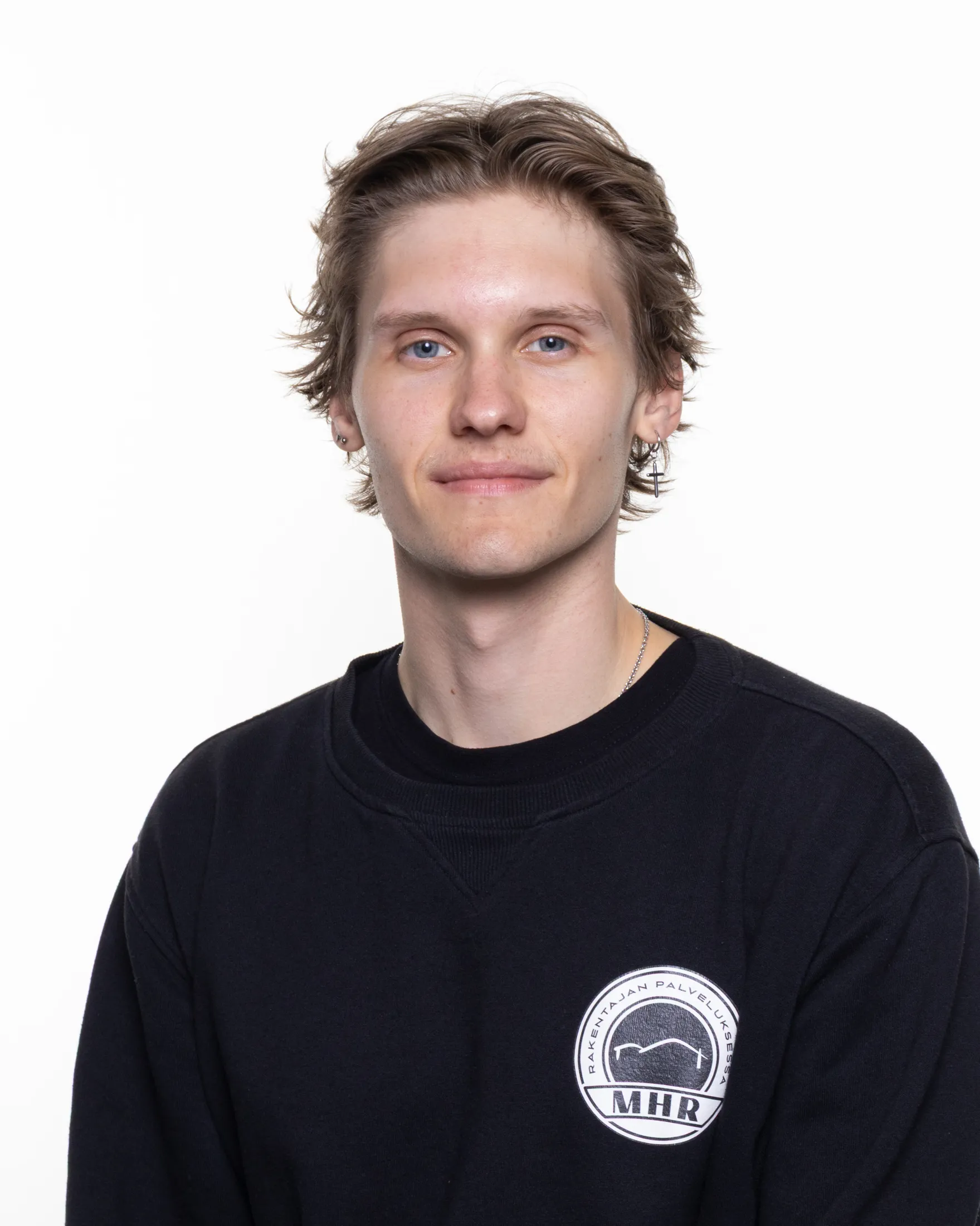 Muotokuva nuoresta miehestä, jolla on vaaleat hiukset, siniset silmät ja musta pusero, jossa on valkoinen logo.